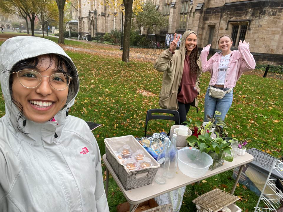 Three students stand in the rain selling baked goods