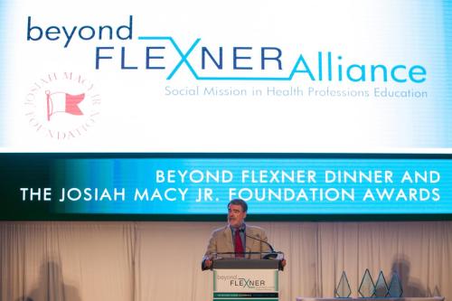 Fitzhugh Mullan speaking at a podium at the Beyond Flexner conference.