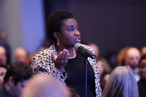 A woman speaks into a microphone in a crowd at the Beyond Flexner conference