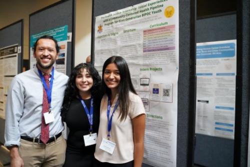 Three students pose in front of a research poster. 